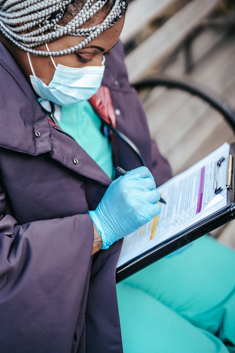 African American Female Doctor Sitting With Papers In Pandemic