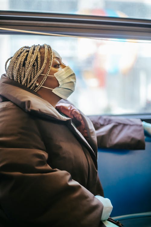 Free Side view of adult black woman in protective mask and gloves wearing warm clothes sitting on bus in daytime Stock Photo