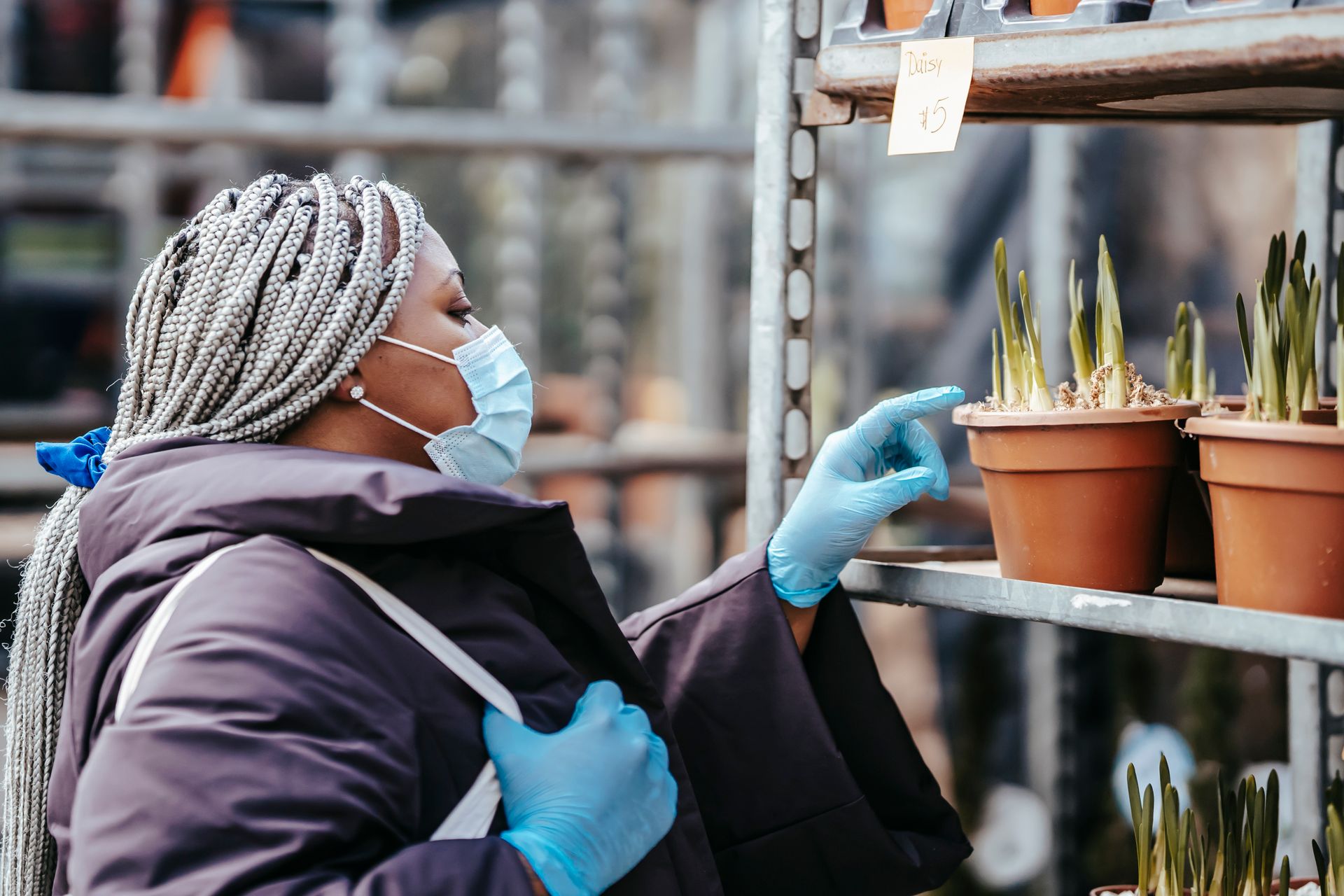 Woman in mask and gloves selecting potted plants outdoors during pandemic.