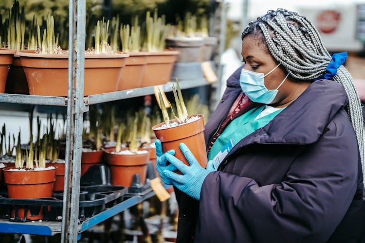 Black Woman Doctor Choosing Plant In Street Market