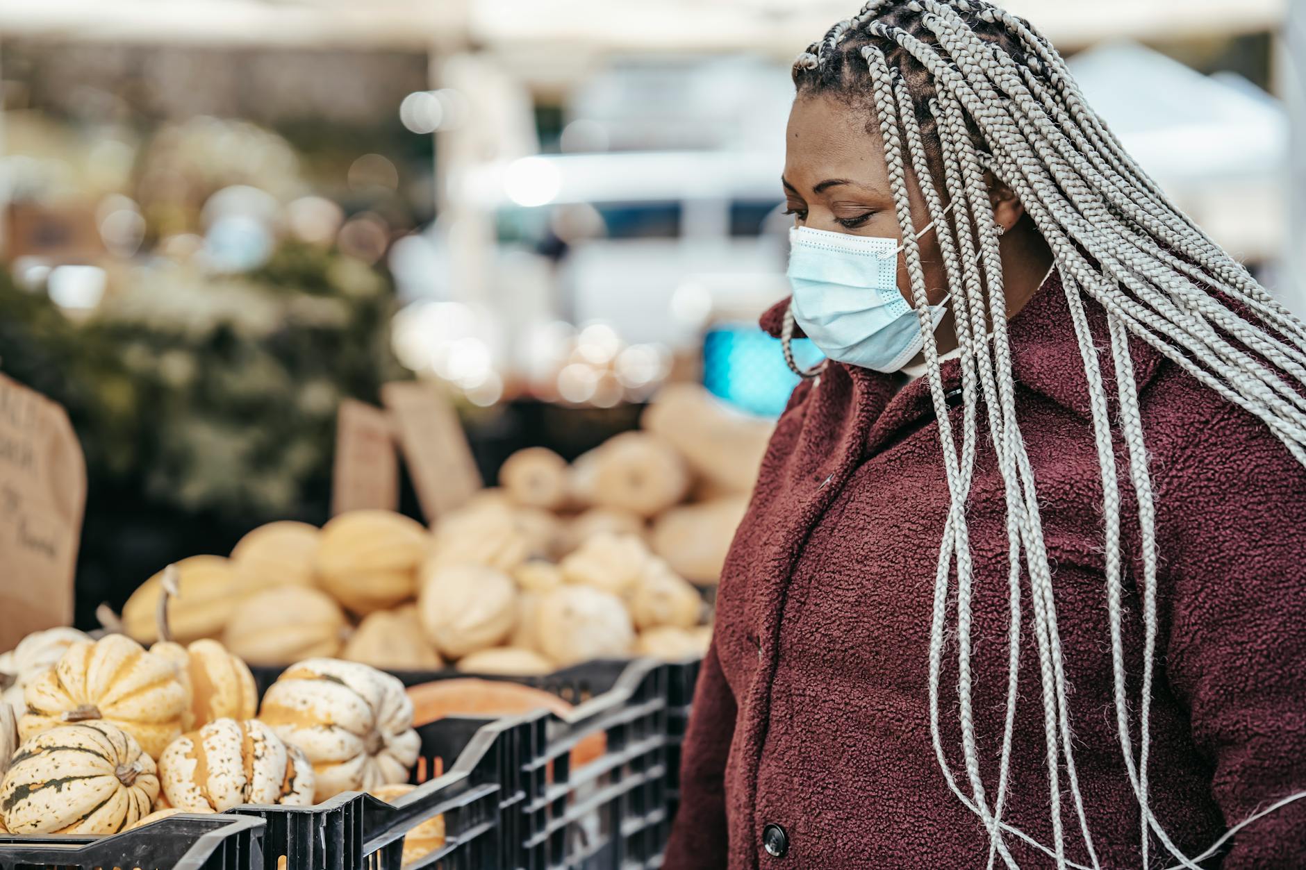 Black woman in medical mask choosing pumpkins in street market