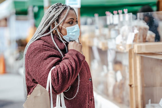 Black woman standing near pastry on market in mask