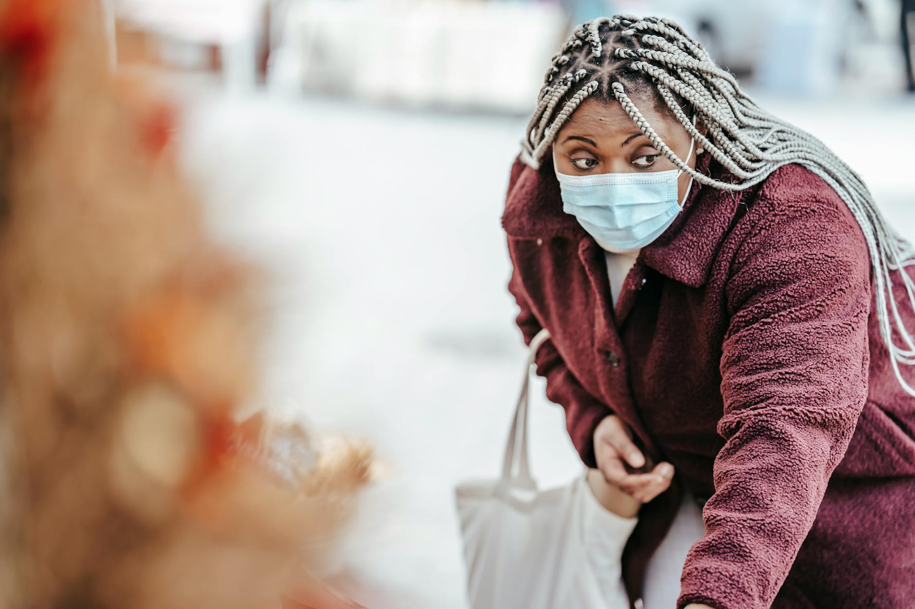 A woman wearing a mask explores items at an outdoor market, focusing on browsing goods.