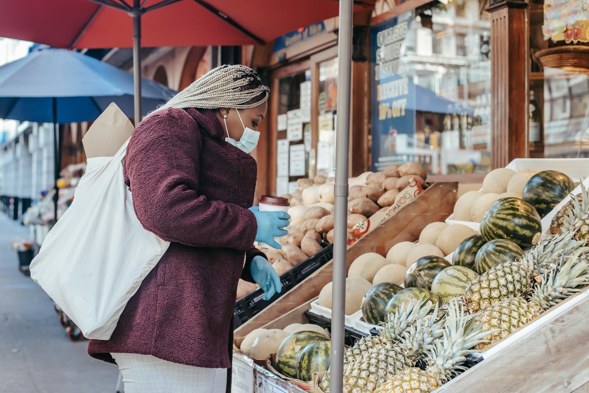 Black woman with coffee picking fruits in stall