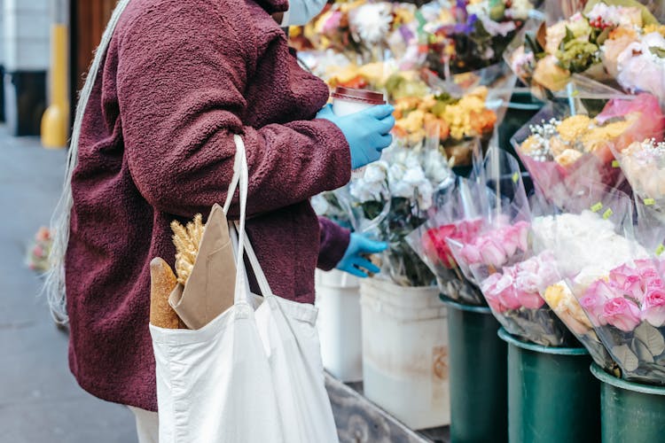 Woman With Paper Cup Of Coffee Buying Flowers On Street