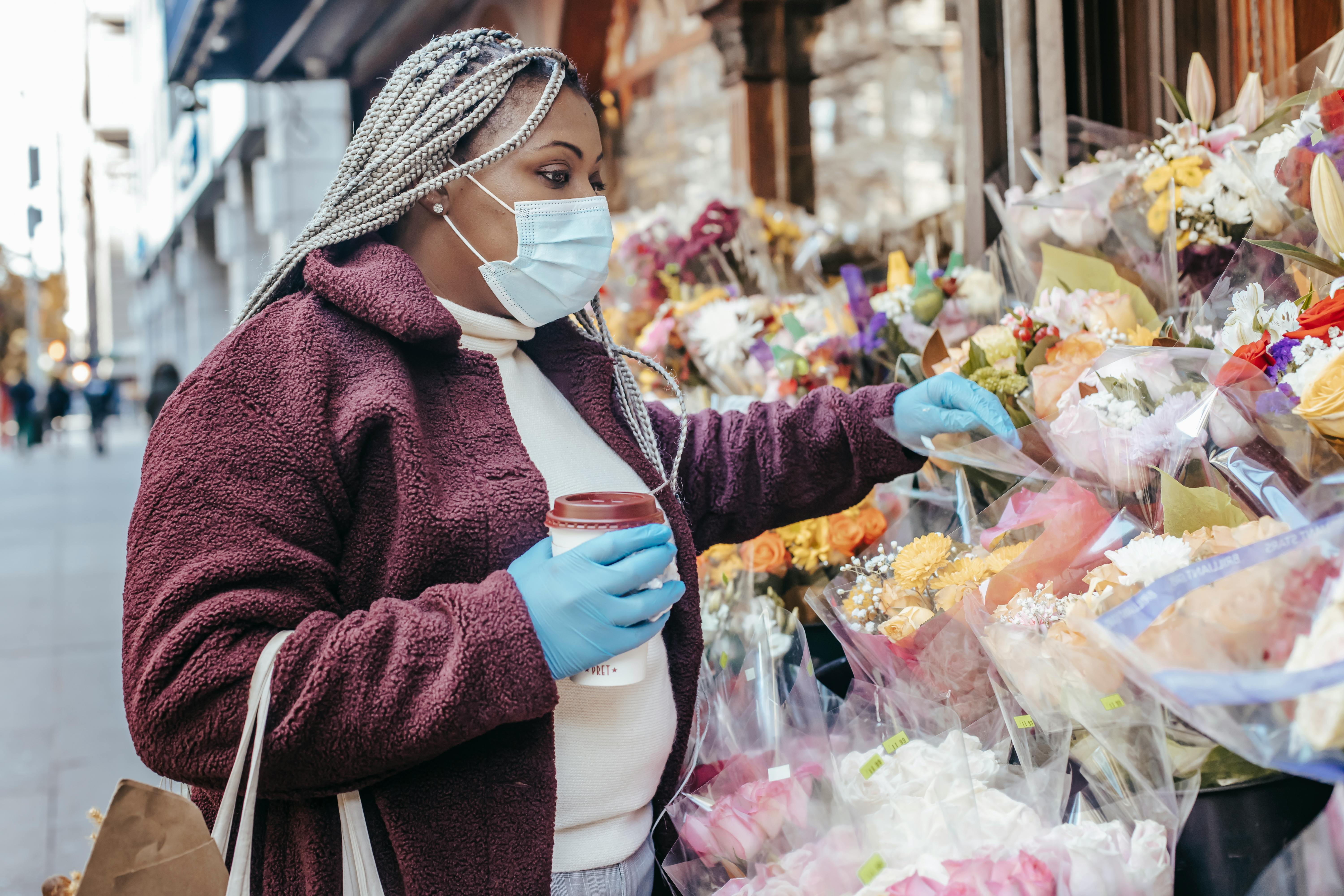 black woman with paper cup of beverage buying flowers on street