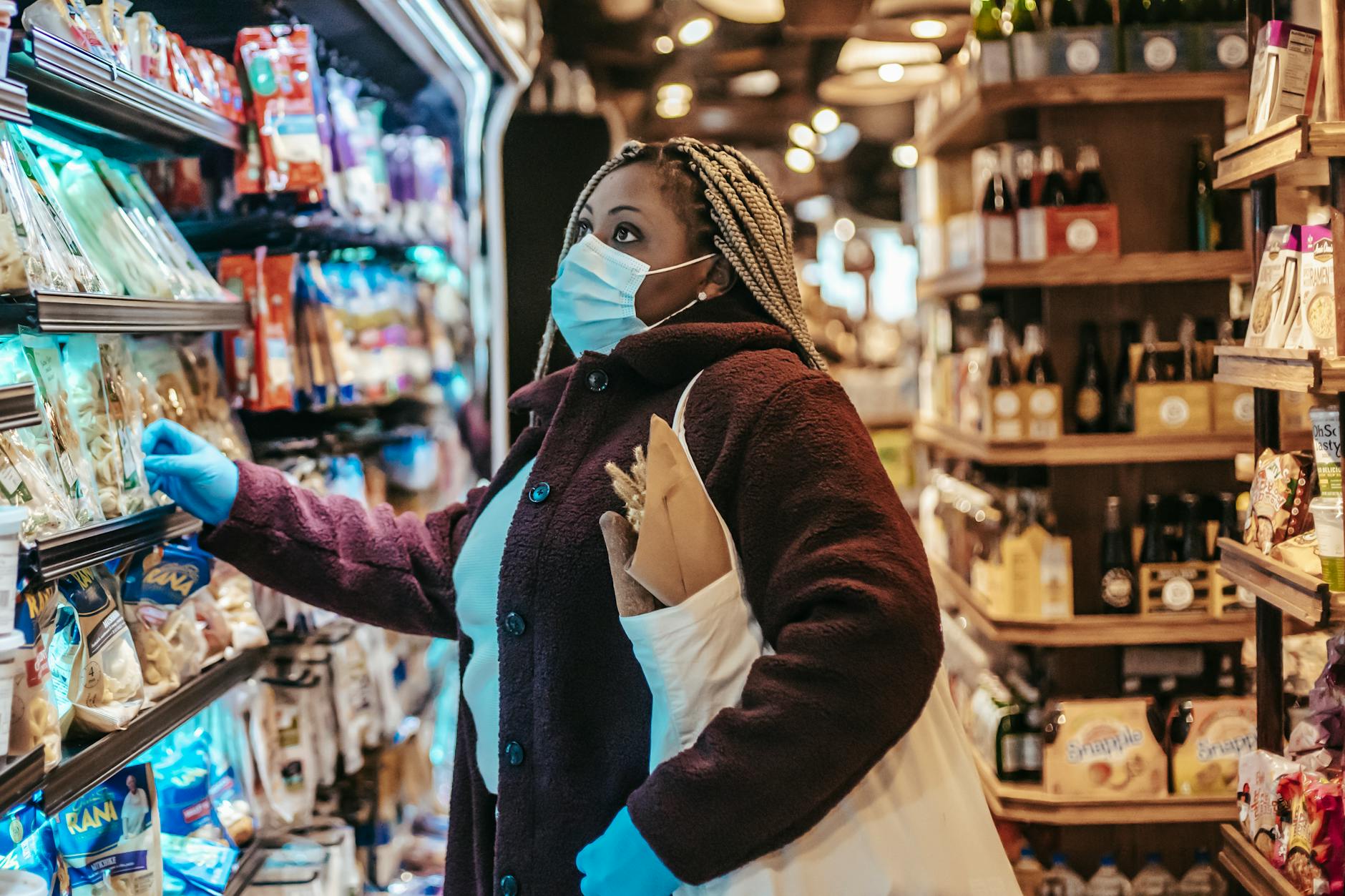 Woman wearing a mask and gloves, shopping in a grocery store during the pandemic.