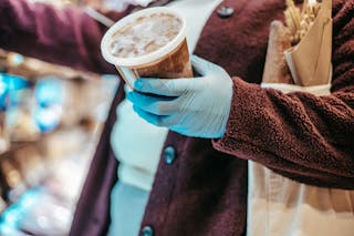 Crop anonymous female buyer in gloves with plastic container of frozen food in grocery store during coronavirus pandemic