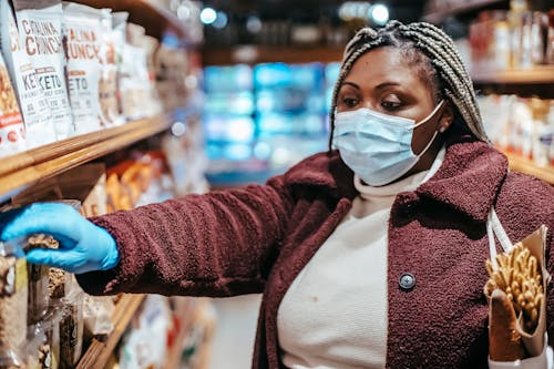 Free African American female buyer in protective mask picking food from shelf in grocery store Stock Photo