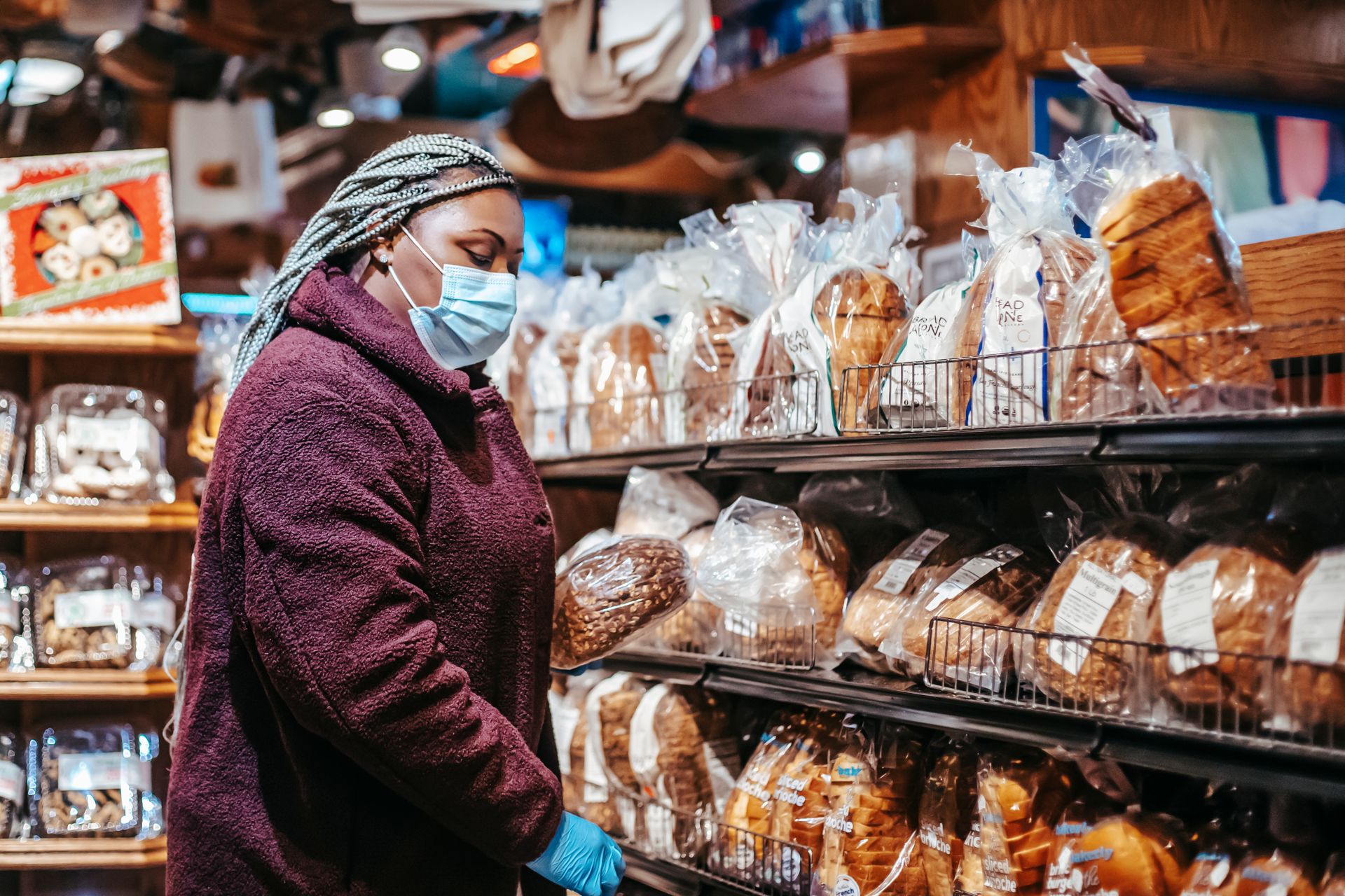 Woman in mask and gloves selects bread in grocery store during pandemic.