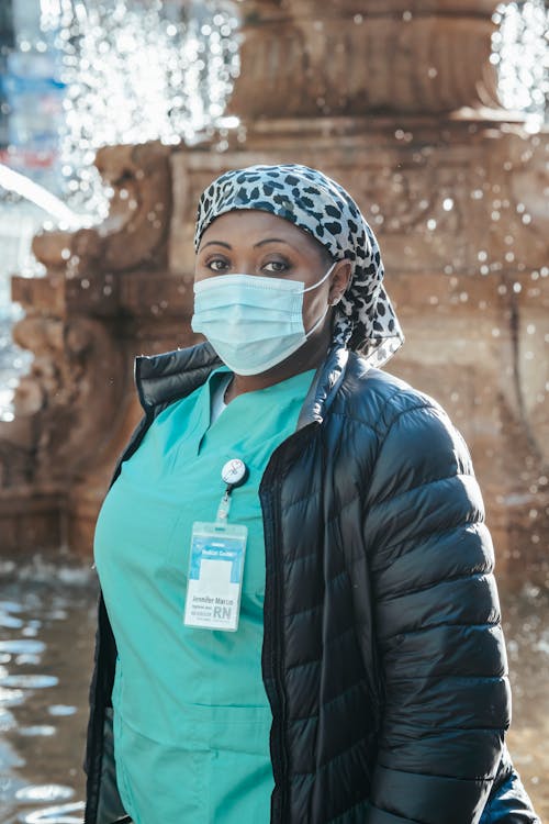 African American woman in medical mask and uniform standing near fountain during break in work