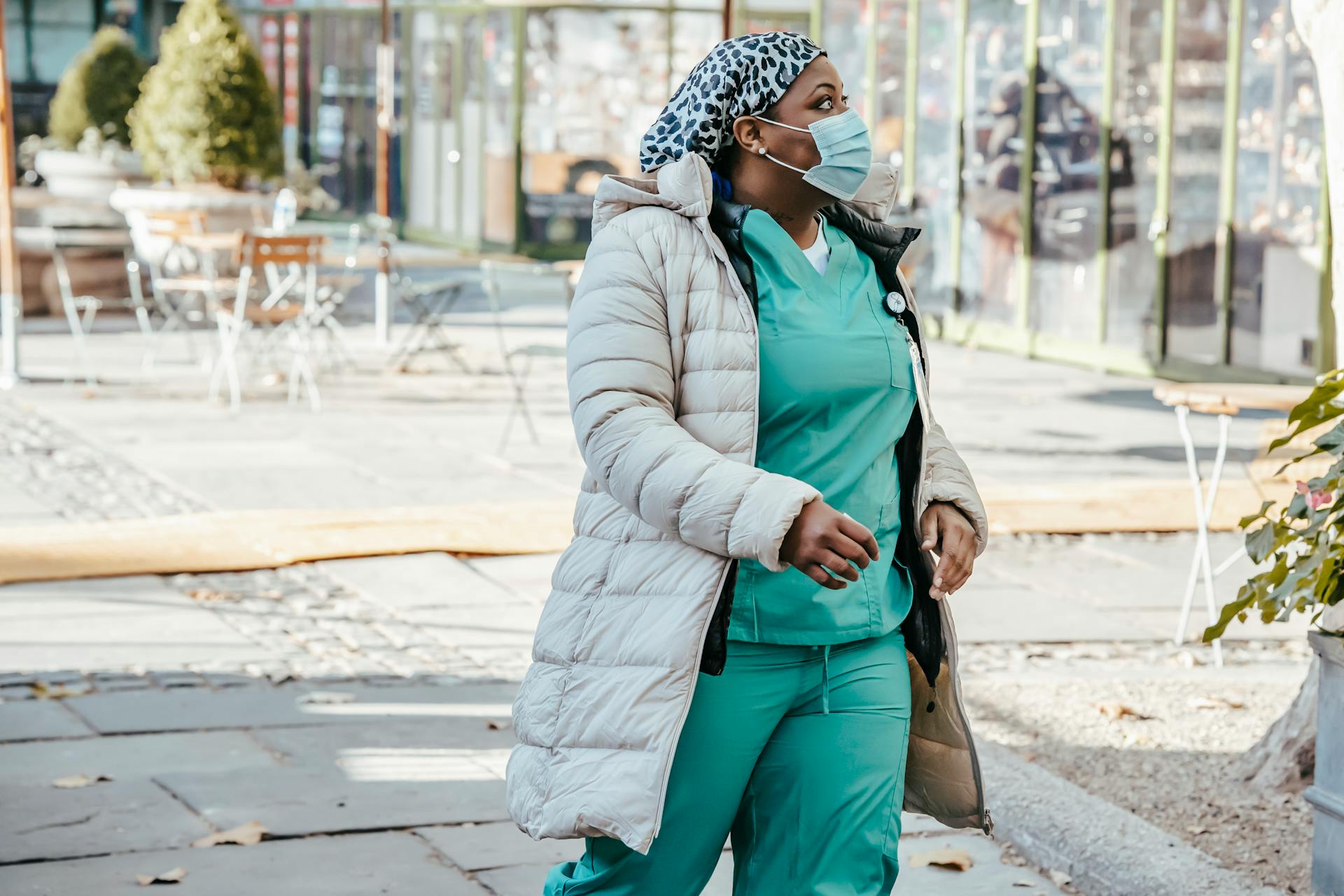 A healthcare professional wearing scrubs and a face mask walks outdoors in a city setting.