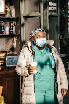 Female nurse in scrubs and mask enjoys a coffee break outdoors during work.