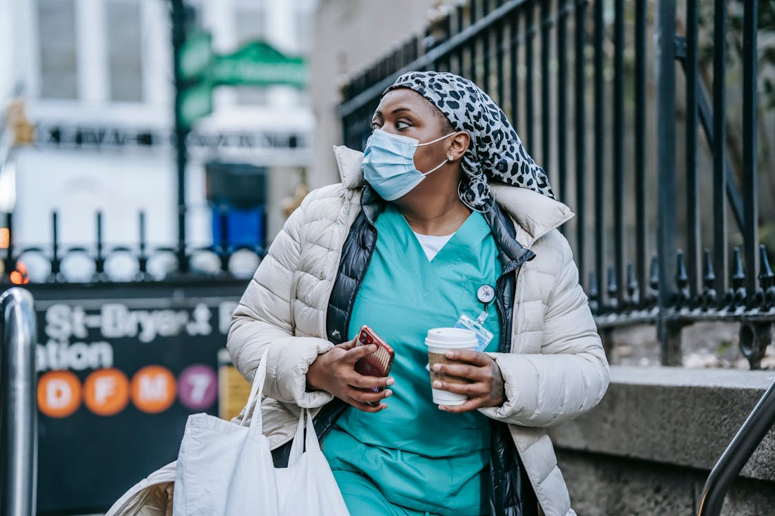 Adult black nurse with takeaway coffee leaving metro station