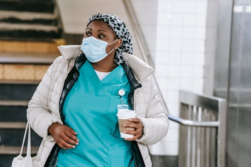 Adult black nurse in outerwear walking in hallway
