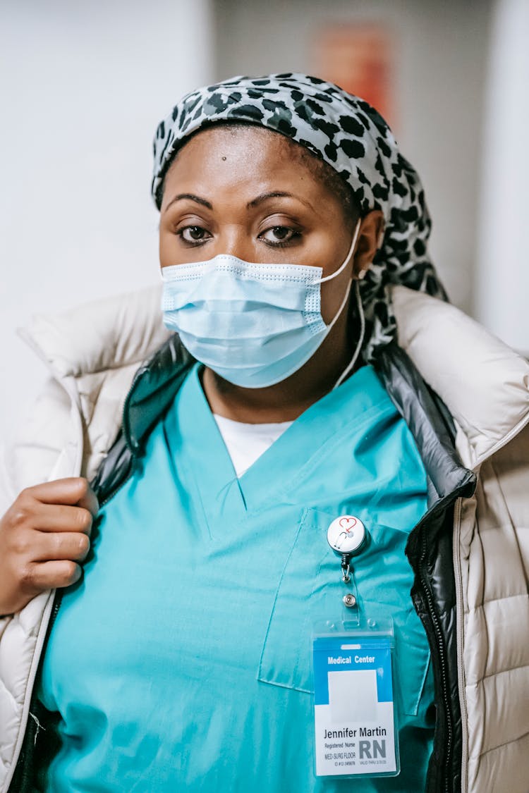 Serious Black Nurse In Mask Standing In Hallway