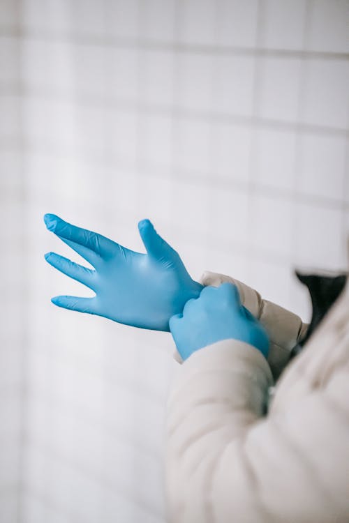 Crop anonymous person wearing warm clothes putting on latex gloves while standing in public place hallway