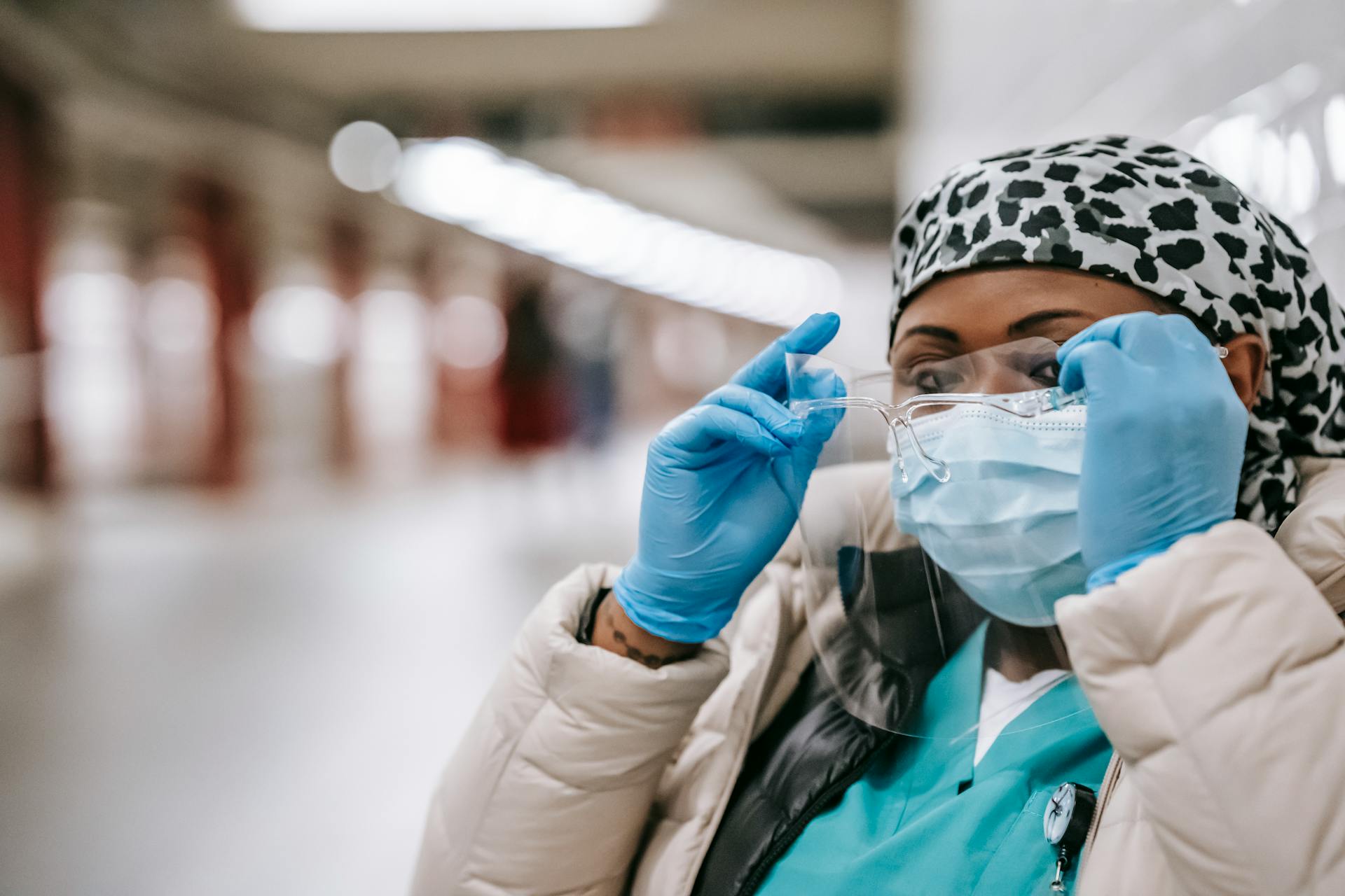 Black nurse in mask and gloves putting on face shield