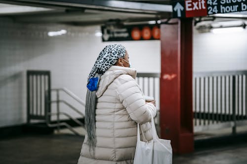 Faceless female in sterile mask walking through underground passage with paper cup of beverage