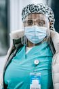 Serious African American female medic in sterile mask and glasses standing in hospital and looking at camera