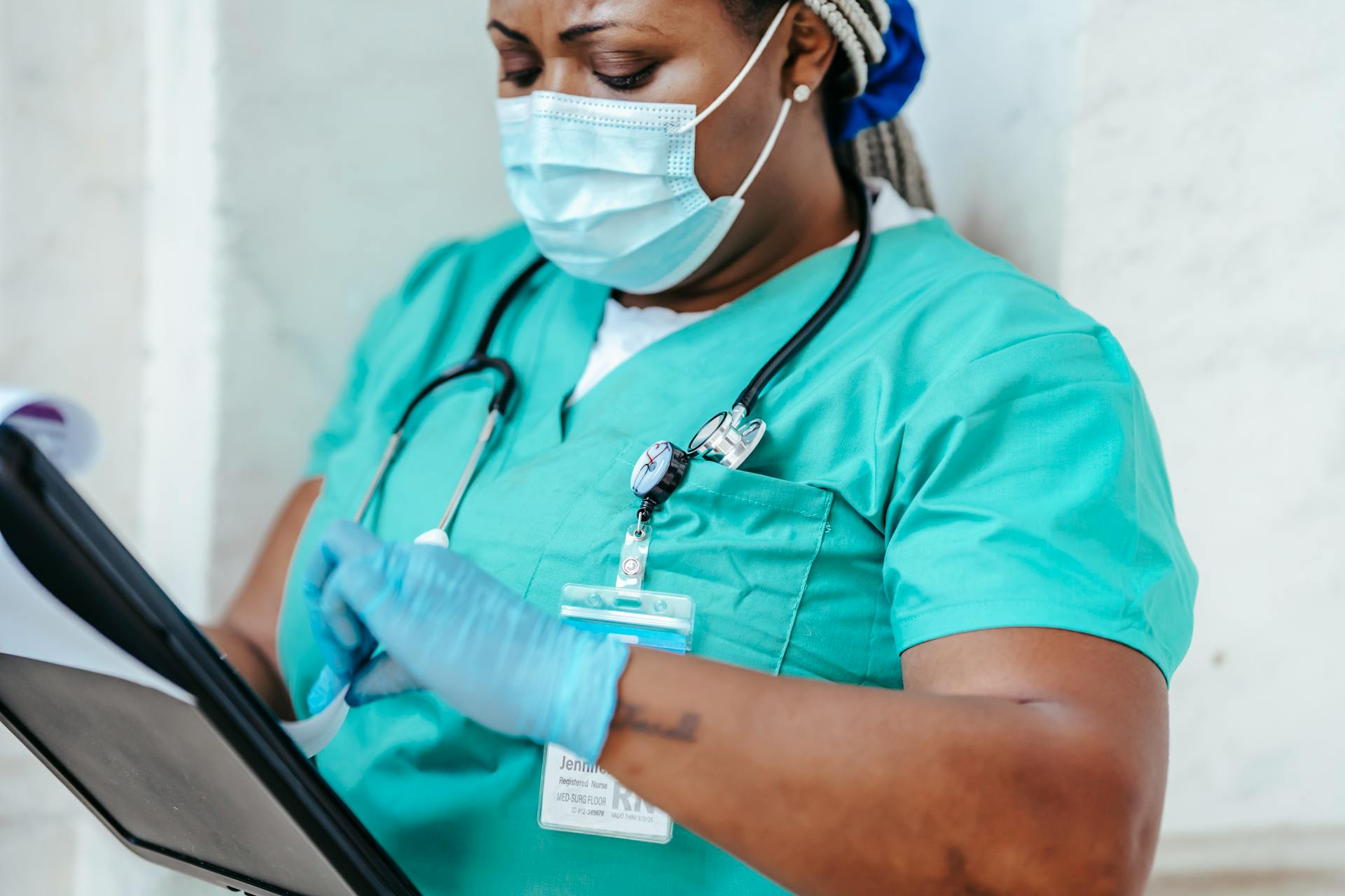 Crop African American woman in uniform standing in hospital and reading patient card while working