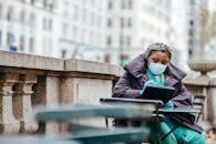 Focused African American woman in protective mask and gloves sitting at table and writing information in balcony