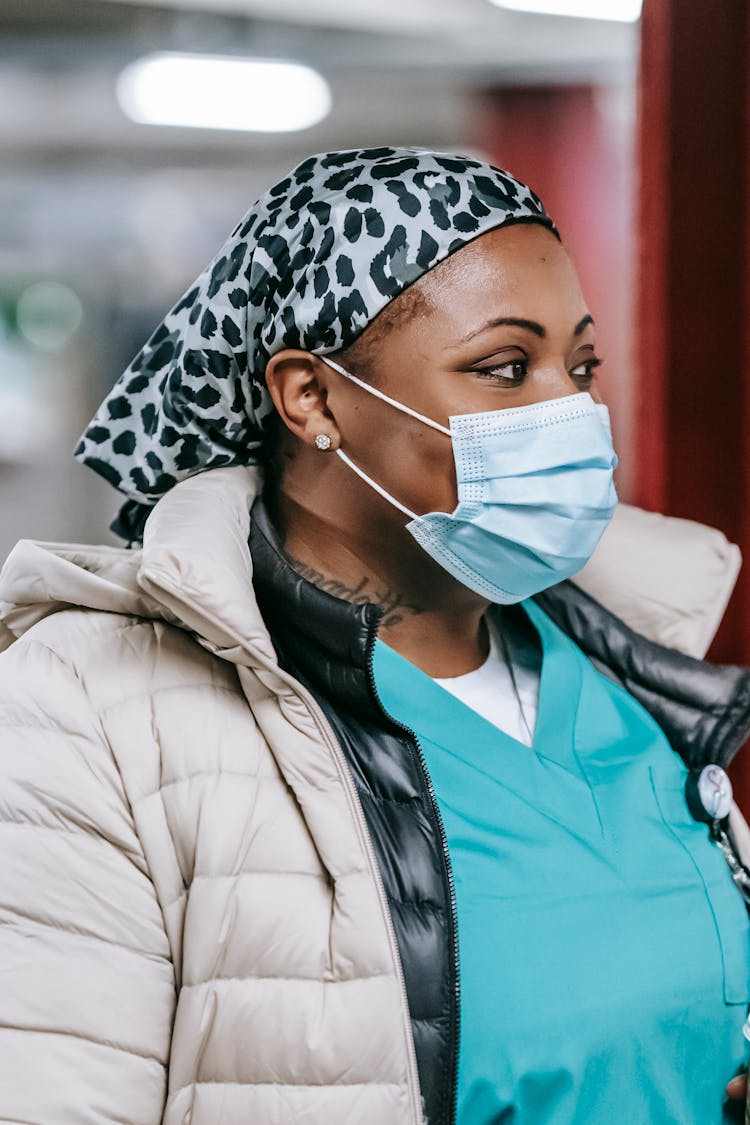 African American Doctor In Medical Mask Looking Away Against Blurred Background