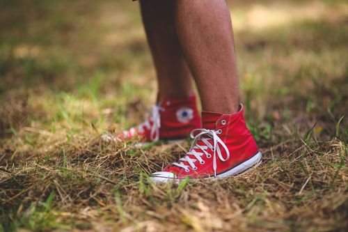 Free A person wearing red Converse sneakers stands on a grassy field, showcasing casual outdoor style. Stock Photo