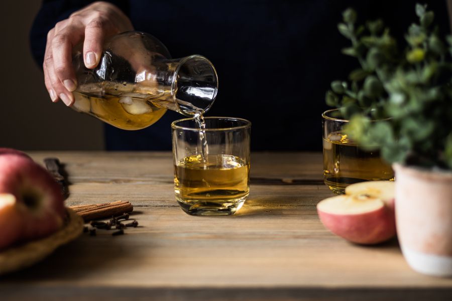 Cider poured from a carafe beside apples on dark wood