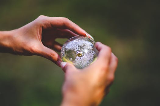 Detailed view of hands holding a crystal ball, capturing light and reflections outdoors.