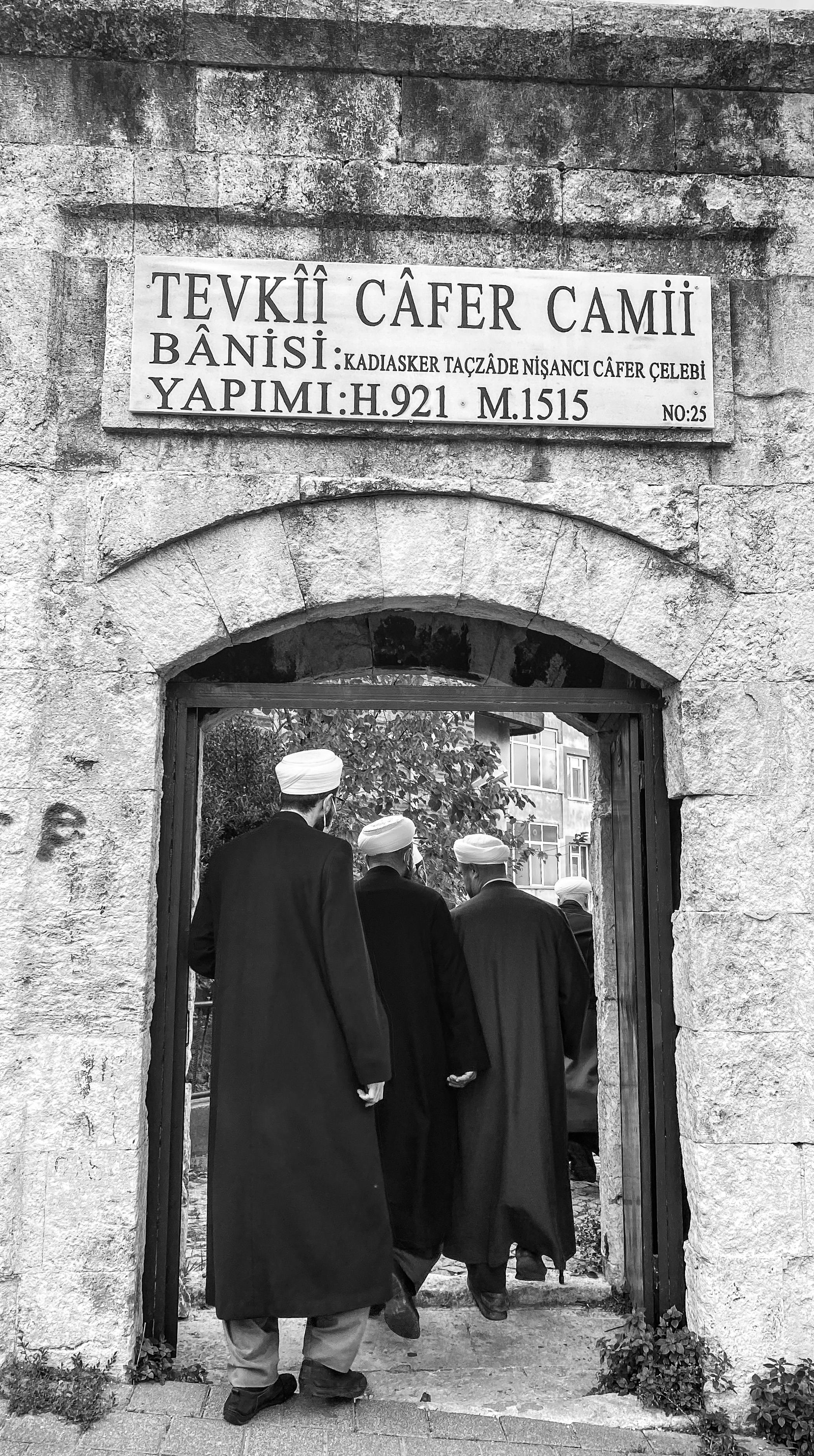 Men entering the historical Tevkii Cafer Mosque in Istanbul through an ancient stone doorway.