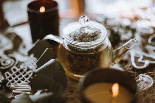 Clear Glass Teapot Surrounded by Lighted Candles on a Wooden Surface