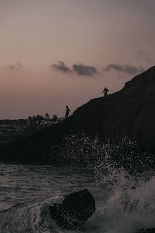 People Standing on Rock Formation Near Sea