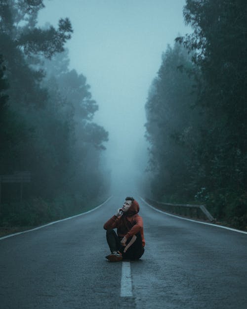 Free Man in Red Hoodie Sitting on Road during Foggy Weather Stock Photo