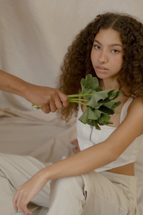 Photo of a Person's Hand Holding Green Leaves Near a Girl with Curly Hair
