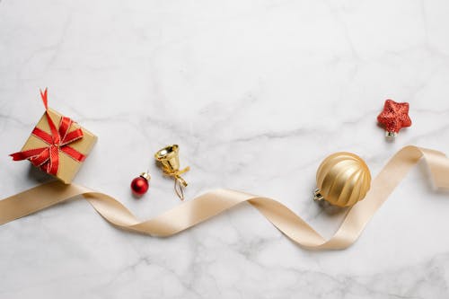 Top view of festive Christmas golden bell with bauble and red star near gift box with shiny ribbon on marble