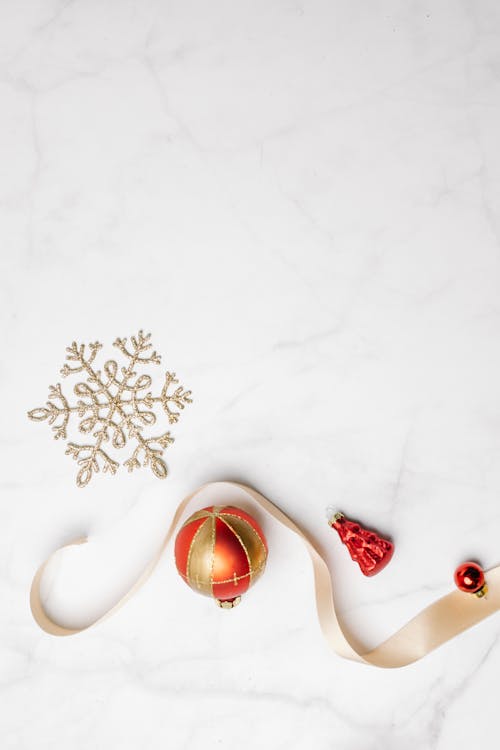Top view of red and golden baubles with ribbon and shimmering snowflake placed on marble surface