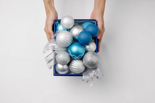 Free Overhead view of crop anonymous person with box full of decorative balls during New Year holiday on white background Stock Photo