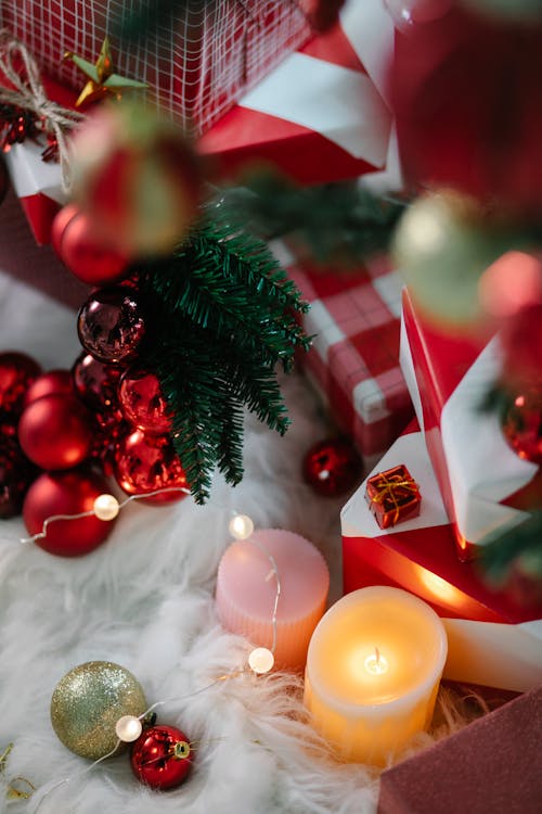 High angle of colorful baubles with shiny garland and flaming candle on soft textile during New Year holiday