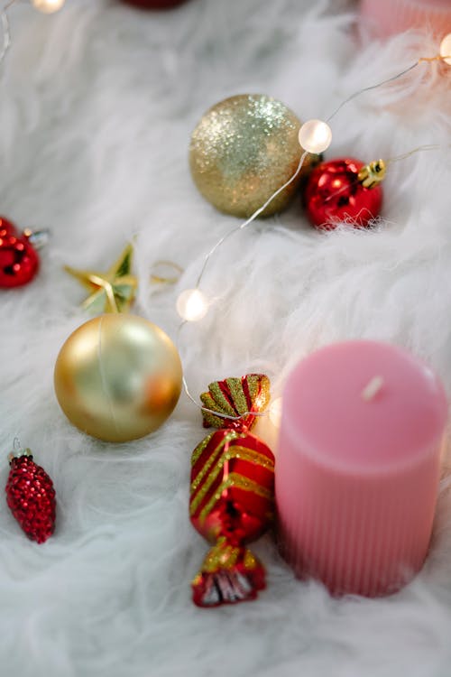 From above of sparkling golden baubles composed with Christmas decorations and candle on fluffy soft blanket