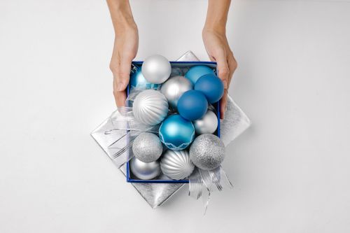 Free Top view of anonymous person with silver and blue Christmas balls on lid present of box placed on white background Stock Photo