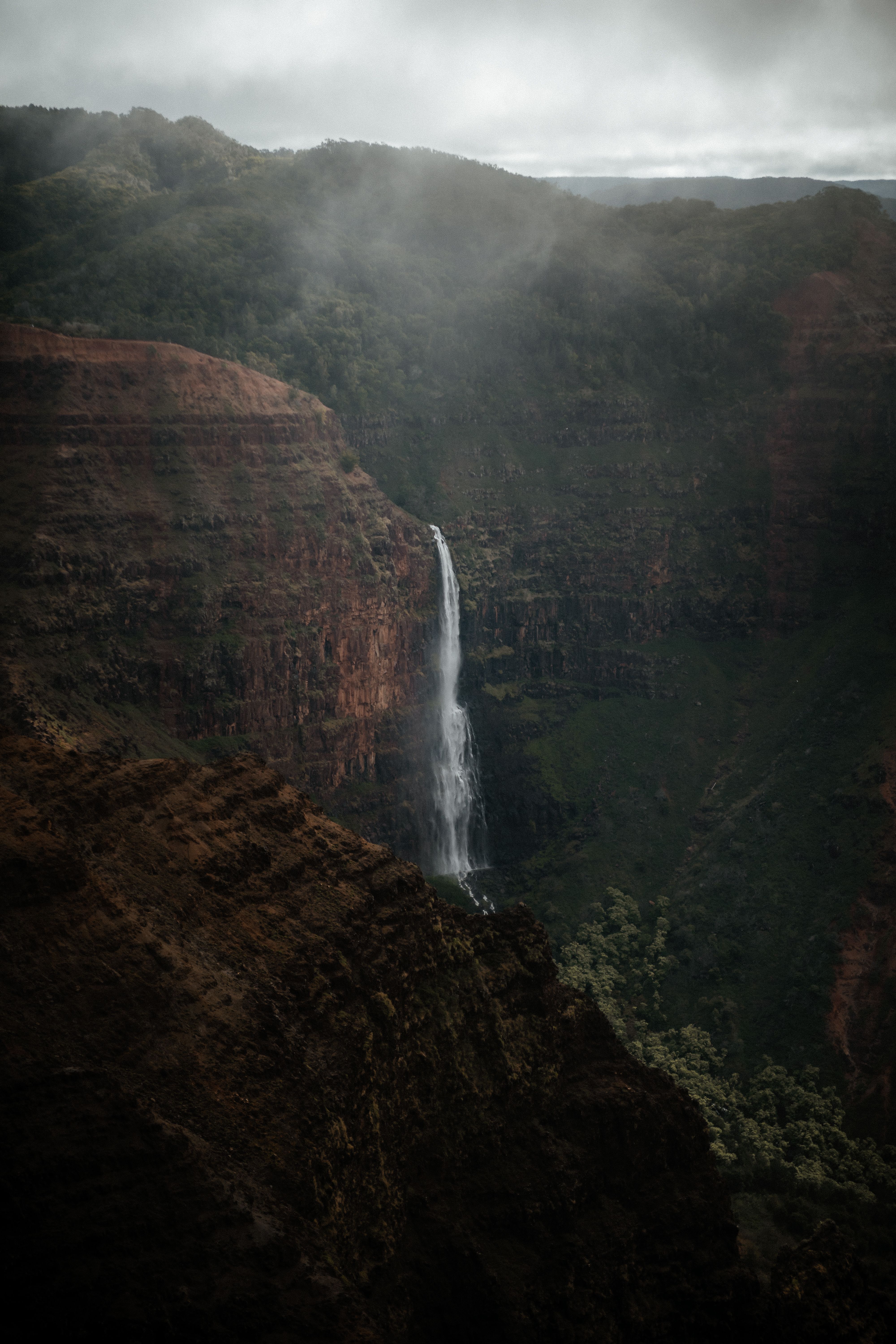 Dramatic view of a waterfall cascading down Waimea Canyon, Hawaii, enveloped by lush green scenery.