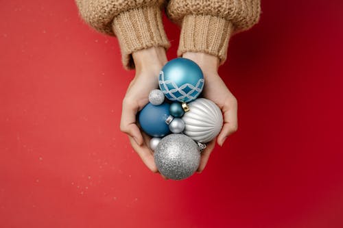 Top view of unrecognizable female in warm knitted clothes holding Christmas tree hanging baubles on red background
