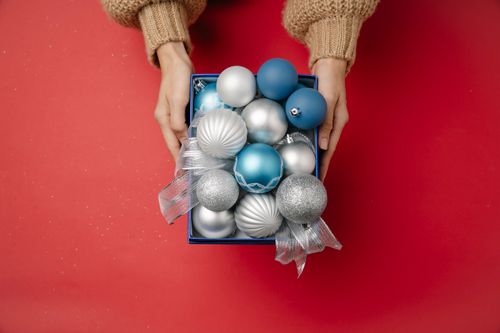 Free Top view of anonymous female with small box filled with Christmas silver blue and pearl hanging baubles and organza white ribbon Stock Photo