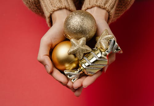 Top view of unrecognizable woman holding in hands Christmas hanging shiny golden baubles