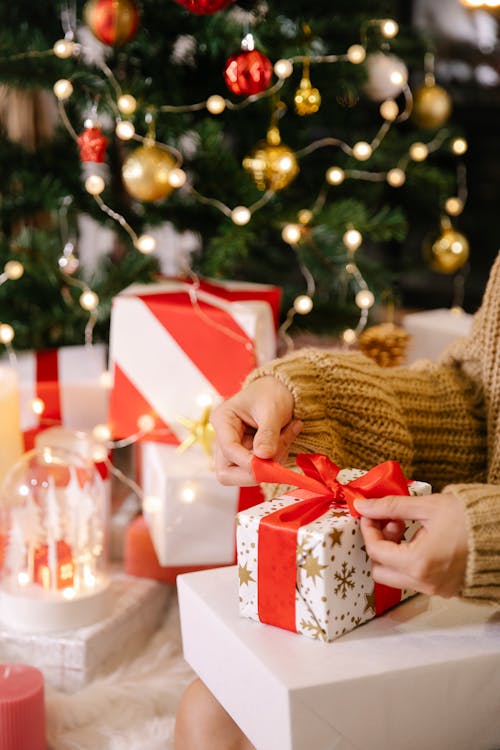 Woman preparing Christmas present near decorated fir tree