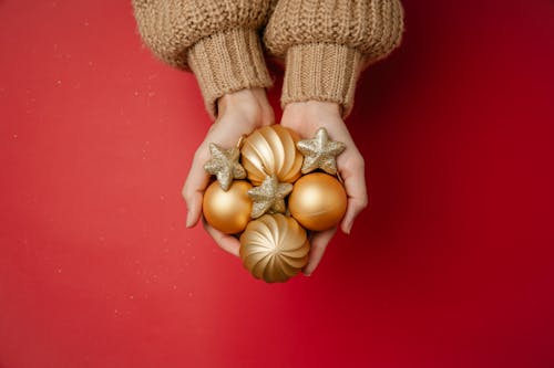 Top view of unrecognizable woman holding heap of golden Christmas ornaments above red background