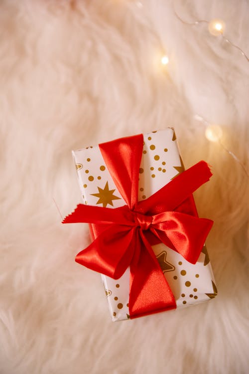 From above wrapped box with Christmas gift decorated with red band and lighted garland