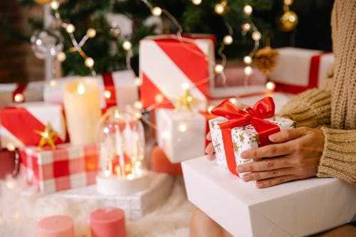 Side view of unrecognizable woman near decorated Christmas tree holding wrapped boxes with Christmas present