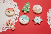High angle of Christmas composition of white doilies and traditional biscuits decorated with colourful icing on red background
